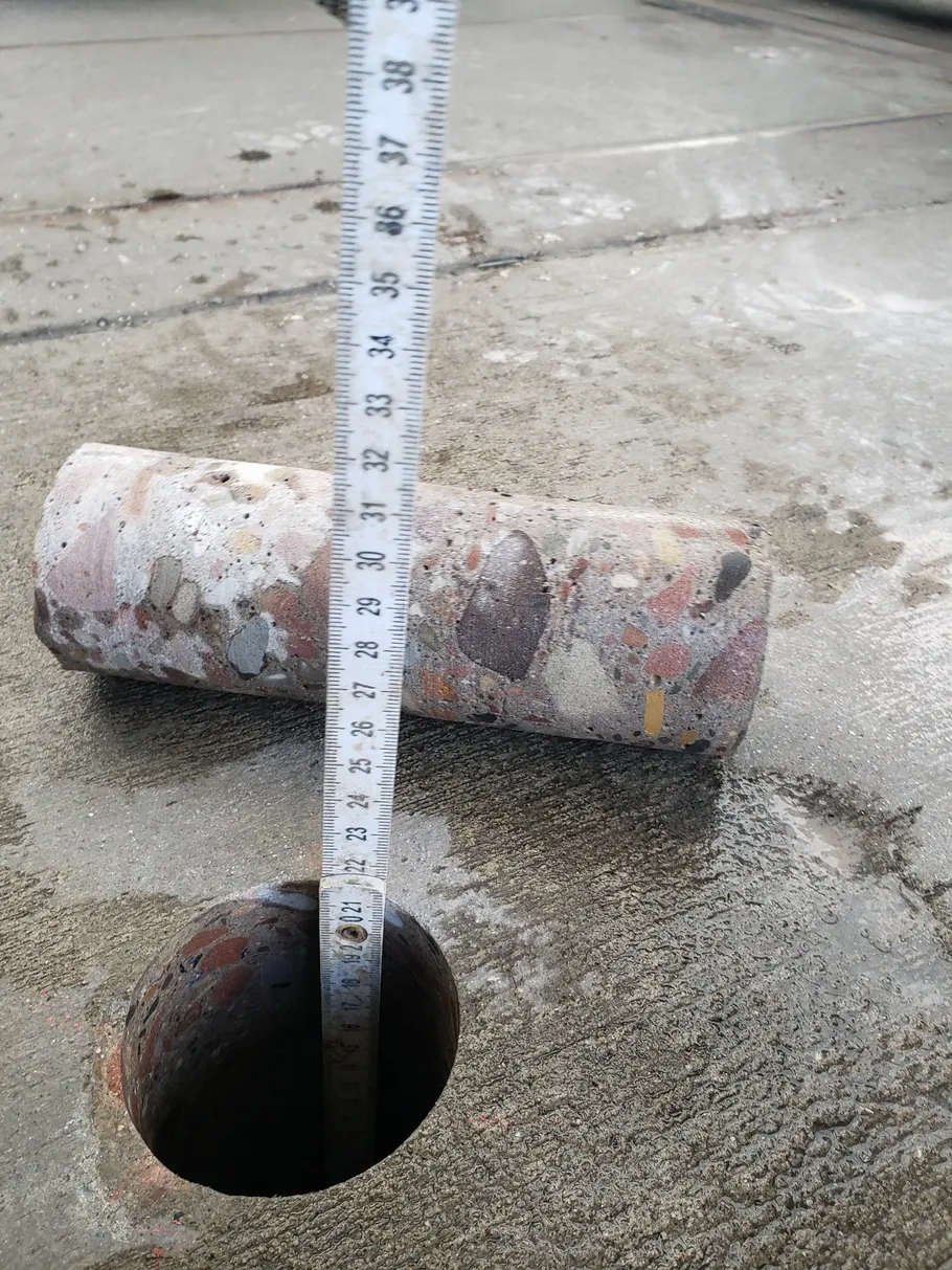 Gezogener Bohrkern liegt neben dem Bohrloch in der Betonsohle, ein Zollstock zeigt den Durchmesser