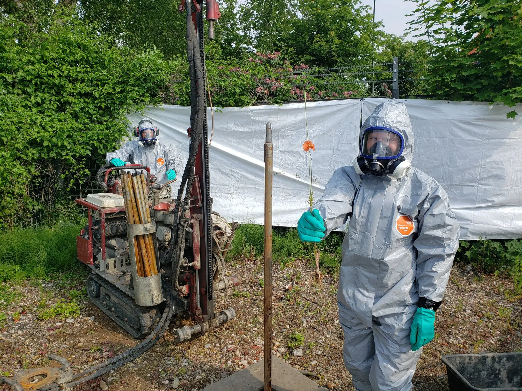 Zwei Mitarbeiter von TERRA V in Schutzanzügen neben dem Bohrgerät im Gelände